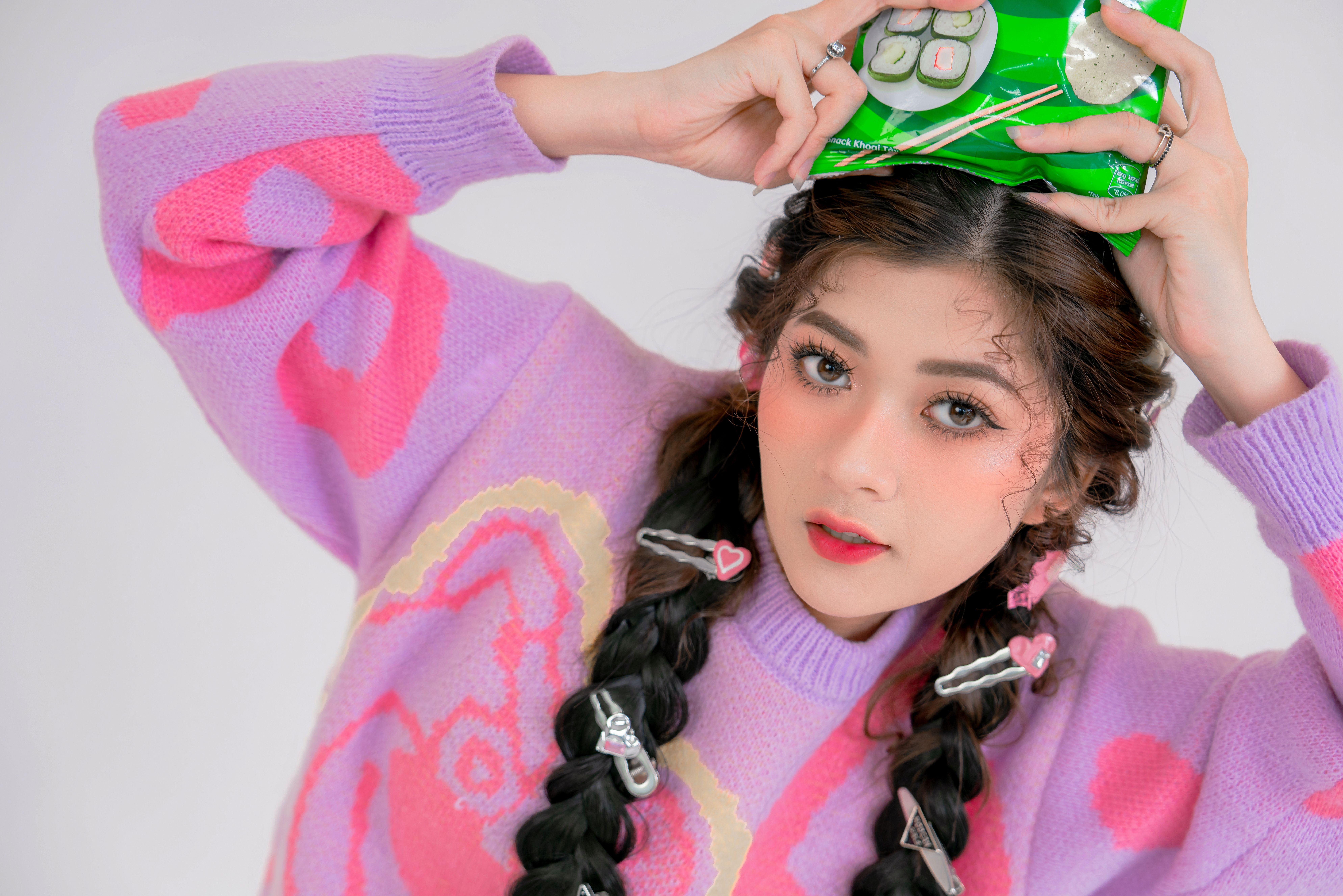 Colorful portrait of a young woman holding snack packaging on her head with playful expression.