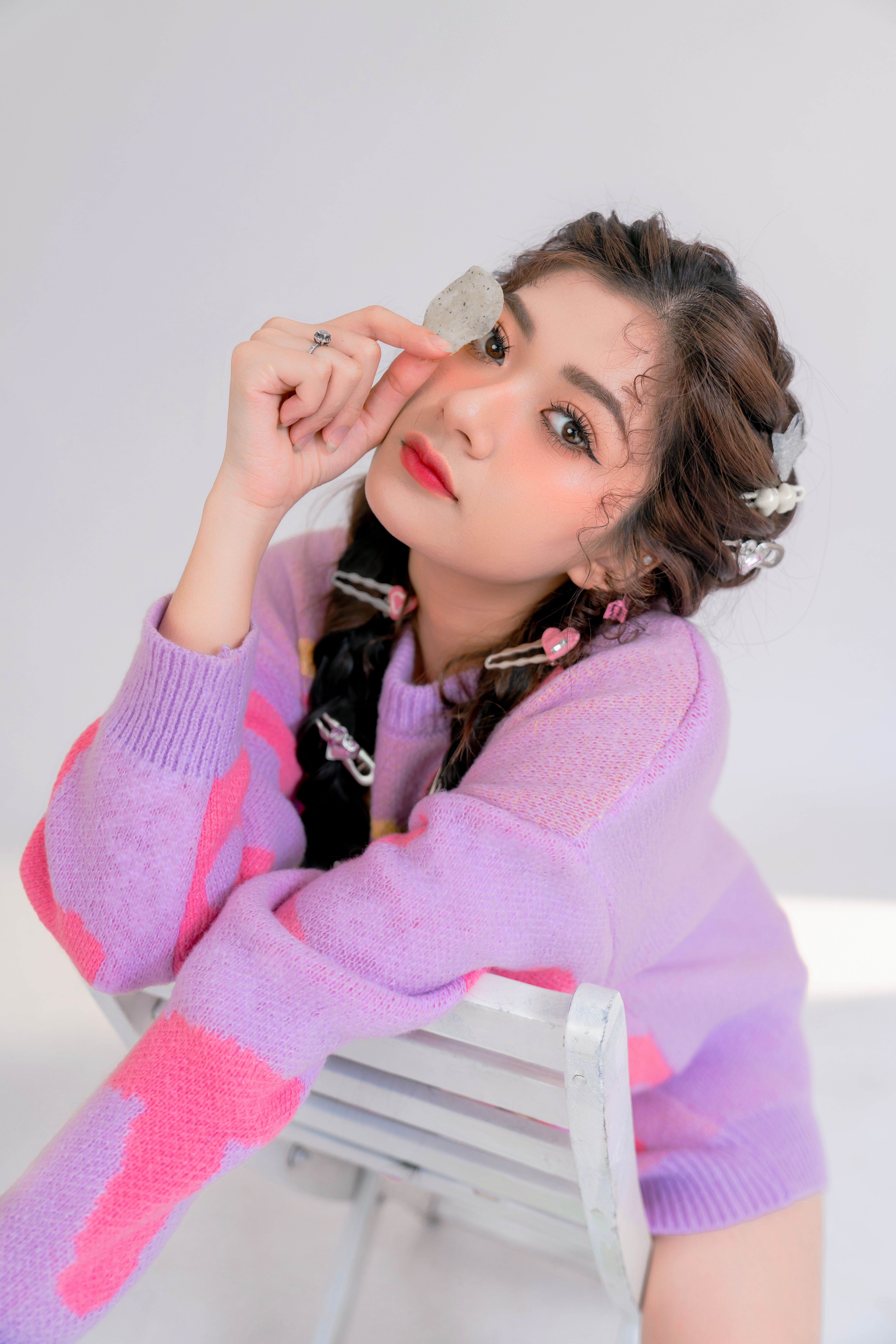 Stylish woman with braided hair, colorful sweater, holding a stone indoors.