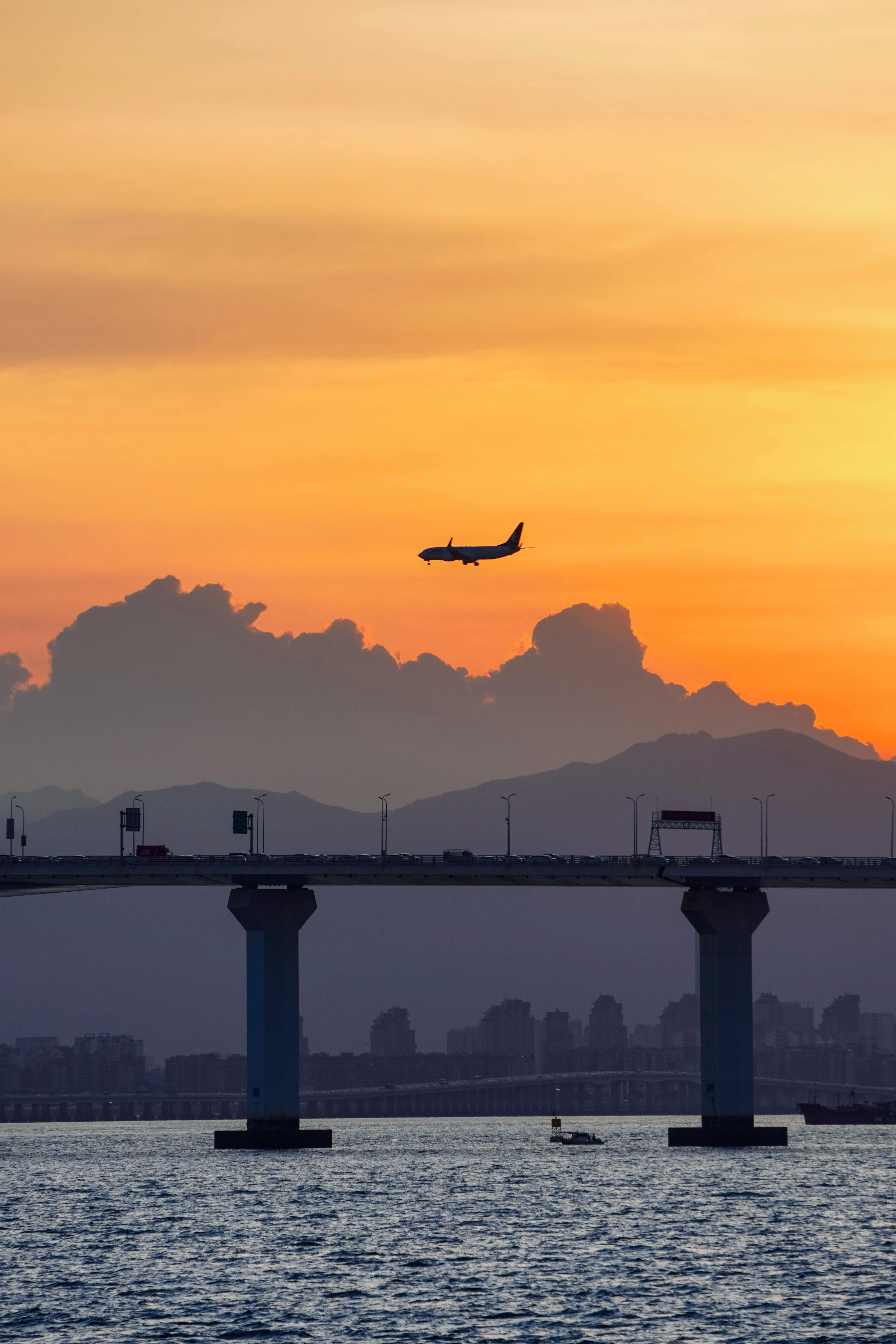 Airplane flying over a bridge with a stunning sunset backdrop, creating a picturesque silhouette.