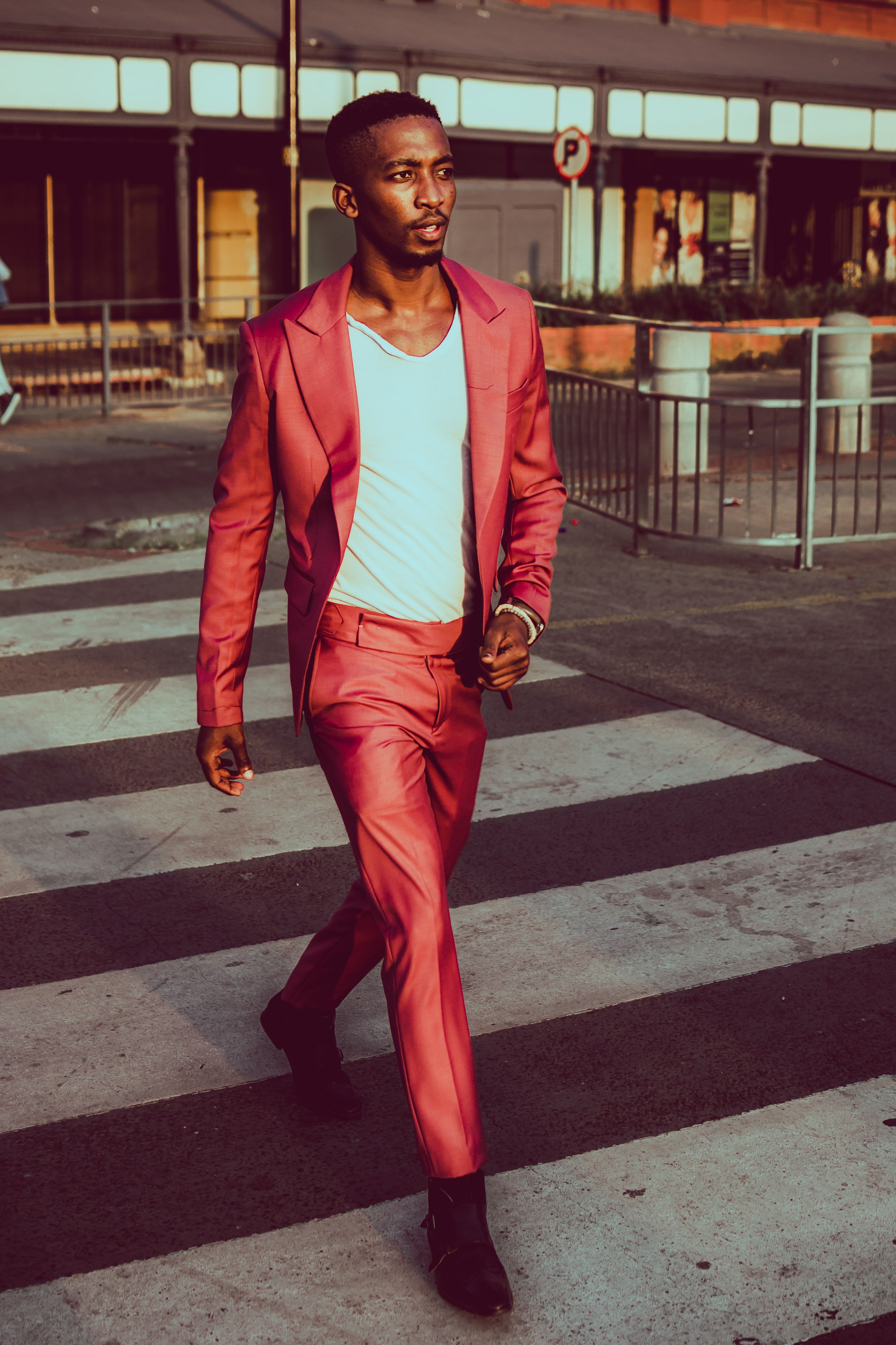Stylish man in a pink suit crossing the street confidently during the day.