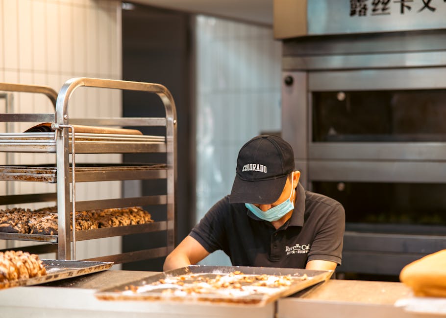 A baker prepares pastries in a commercial kitchen, focusing on fresh baked goods with care.