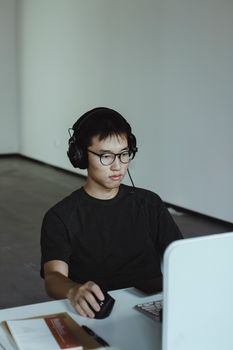 Young man wearing headphones working on a computer at his desk in a modern office setting.