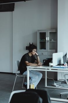 Adult man wearing headphones working at computer in modern office setting.