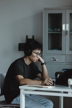 Focused young man with headphones working on a laptop at home office.