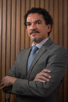 Confident businessman in a suit posing with arms crossed against wooden background.
