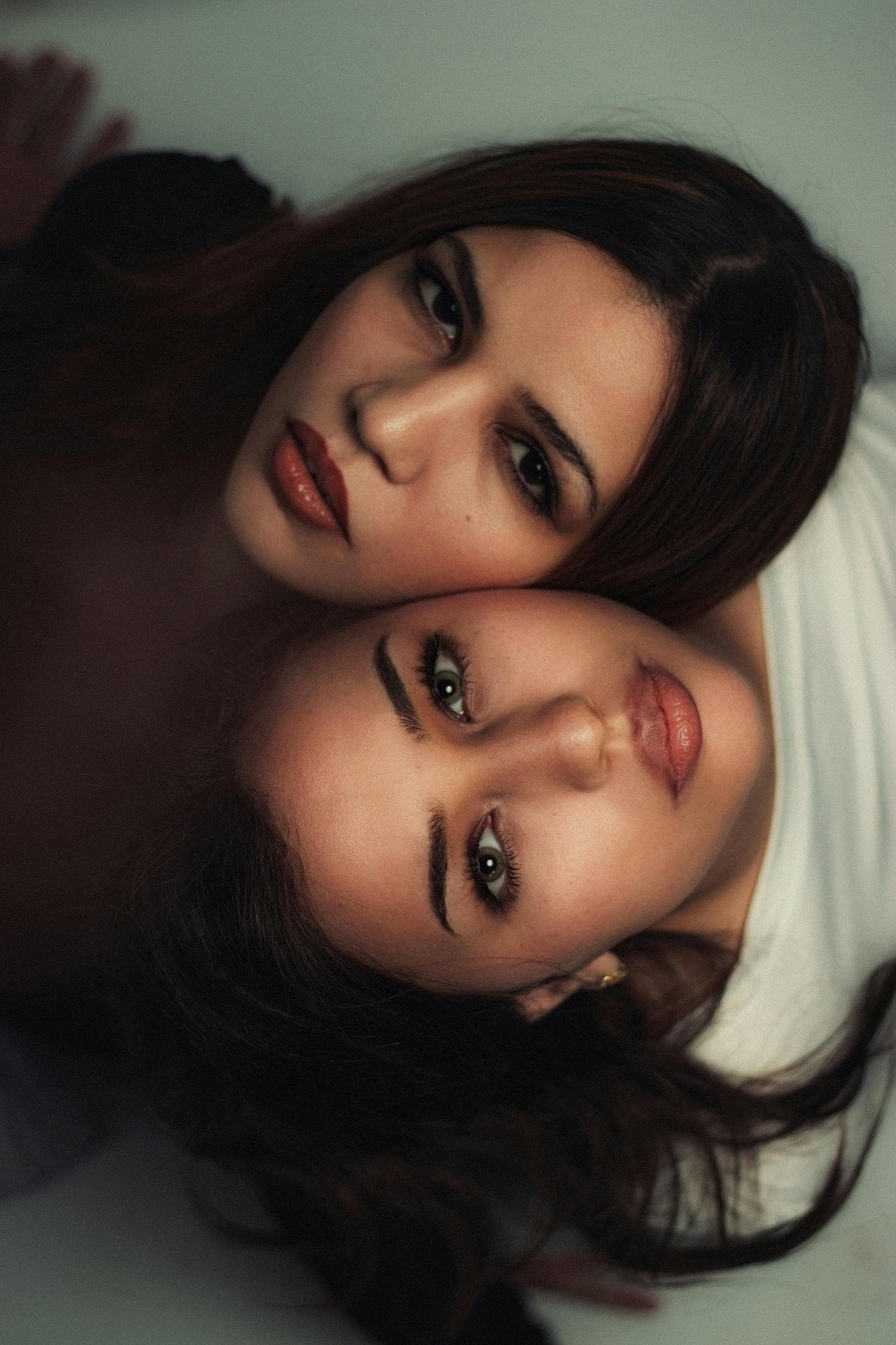 Close-up portrait of two women lying head to head with intense expressions and soft lighting.
