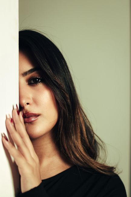 Elegant portrait of a woman partially hidden behind a wall, exuding mystery and style.