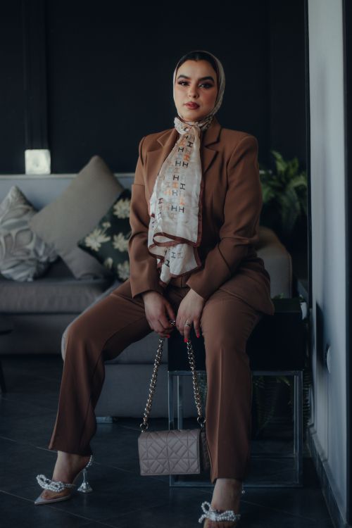 Free Elegant woman in brown suit with hijab sitting indoors, exuding confidence. Stock Photo