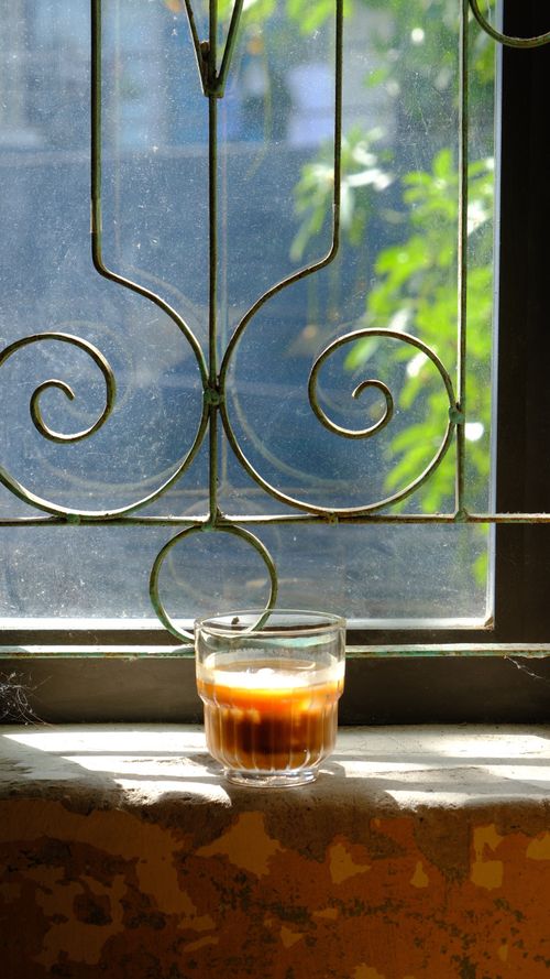 Free A warm cup of coffee on a sunlit windowsill with decorative iron grille. Stock Photo