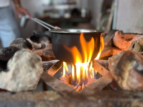A black pot cooking over a vibrant open flame on a rustic stove, showcasing traditional cooking methods.