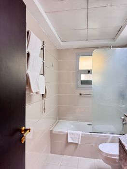 Spacious bathroom featuring tiled walls, bathtub, towels, and minimalistic design.