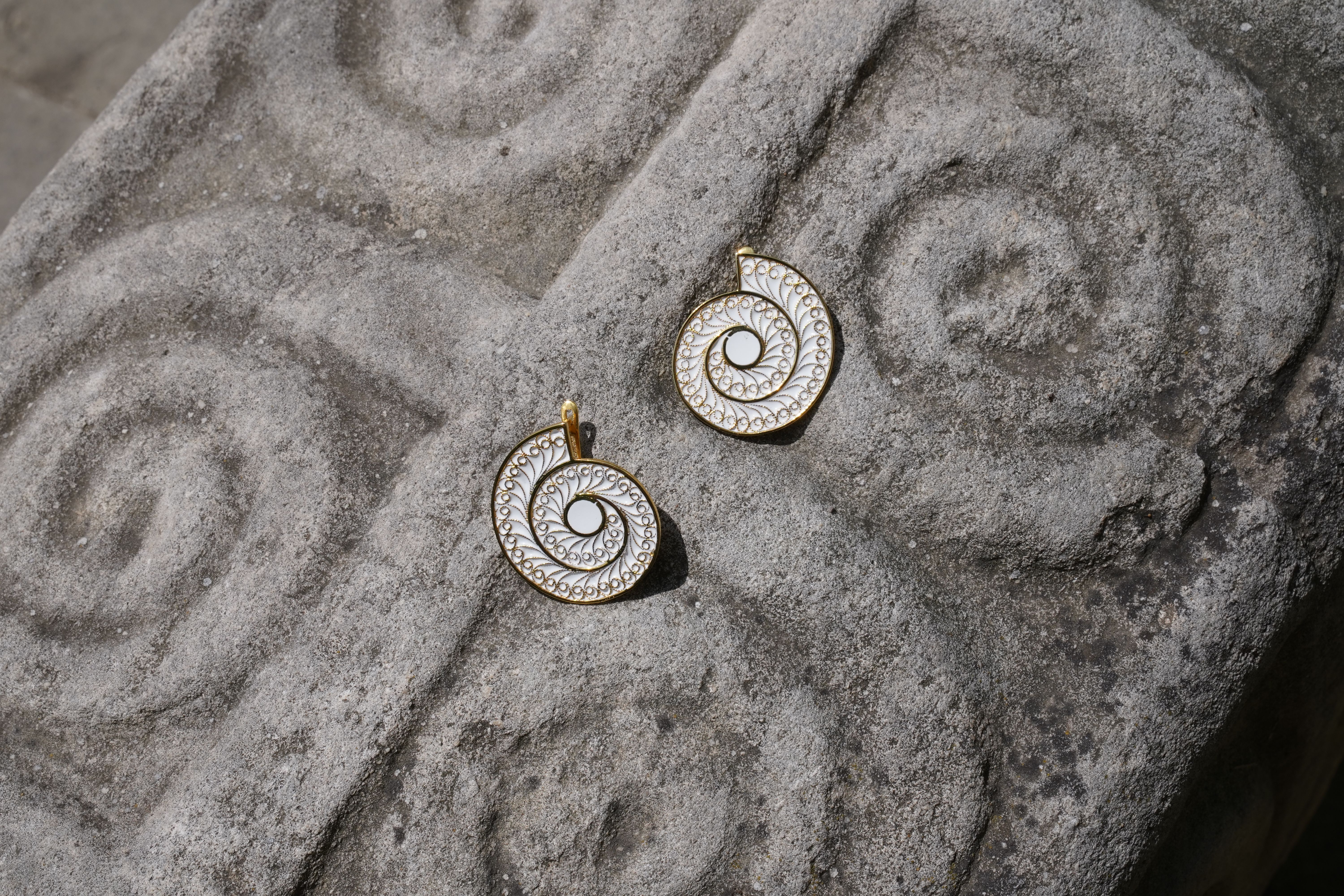 Elegant gold spiral pendants displayed on a textured stone surface, capturing a contrast of modern and ancient design. 
