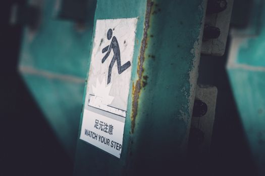 Dimly lit caution sign indicating 'Watch Your Step' in urban setting.