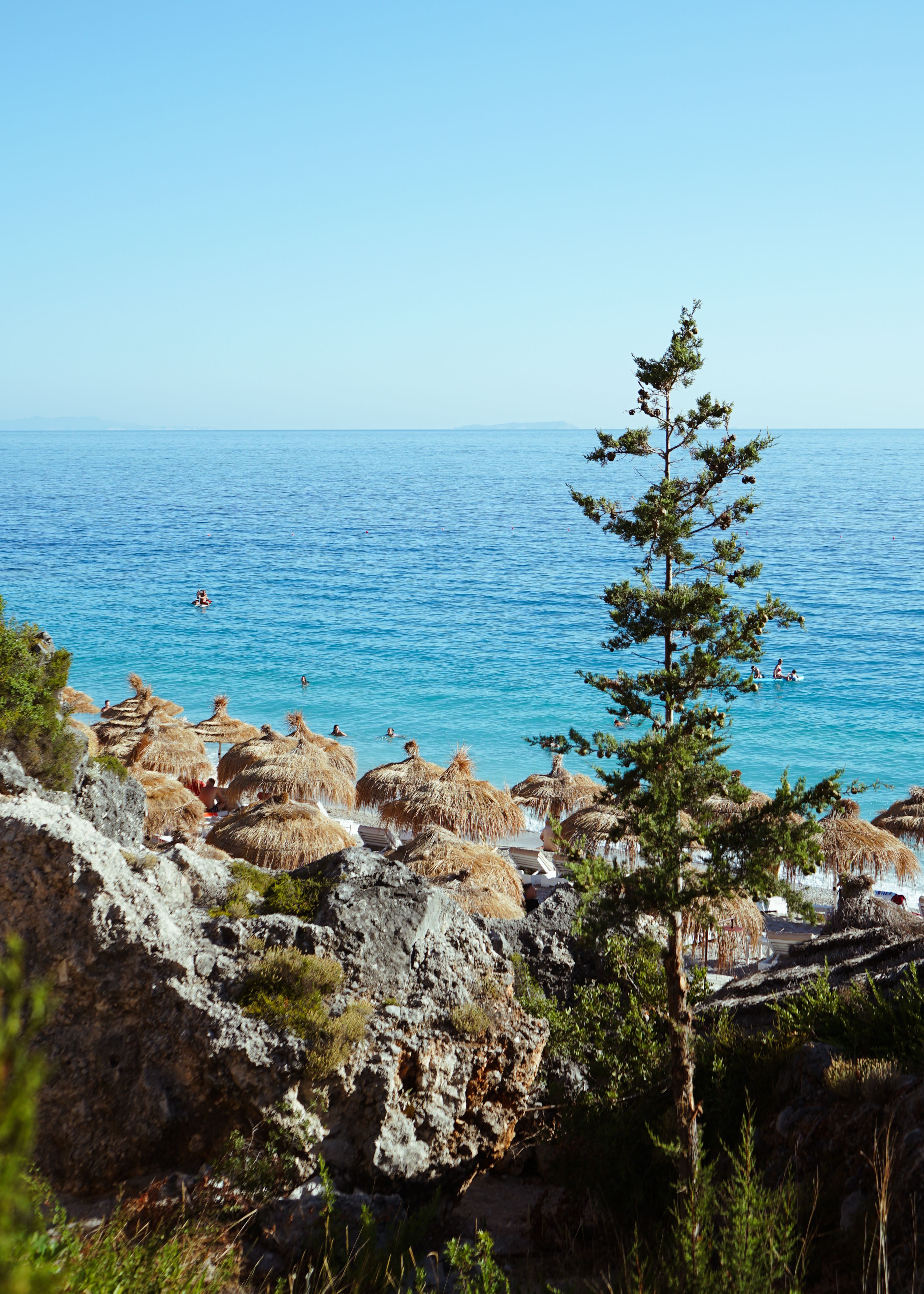 Wide pebble beach and clear blue water backed by green mountains at Dhermi on the Albanian Riviera