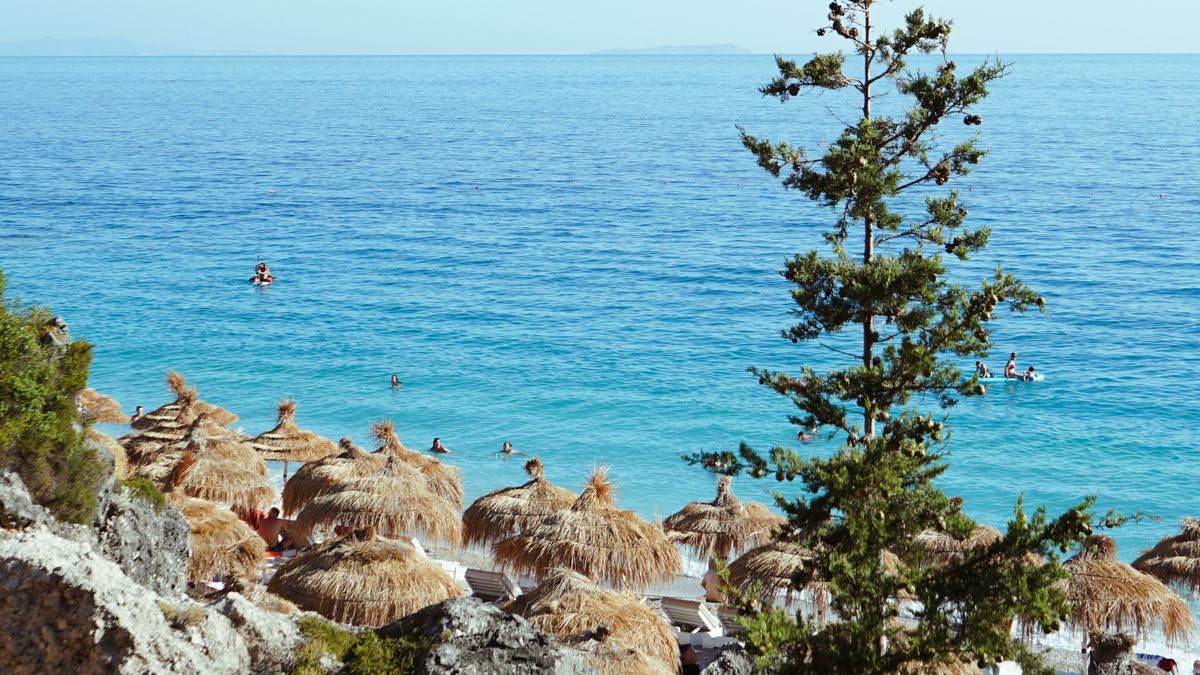 Wide pebble beach and clear blue water backed by green mountains at Dhermi on the Albanian Riviera