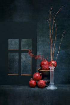 Elegant still life with pomegranates and branches in a vase, against a dark background.