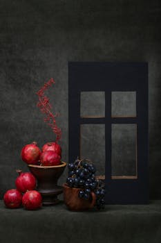 Artistic still life featuring pomegranates and grapes on a dark background, styled with a modern touch.