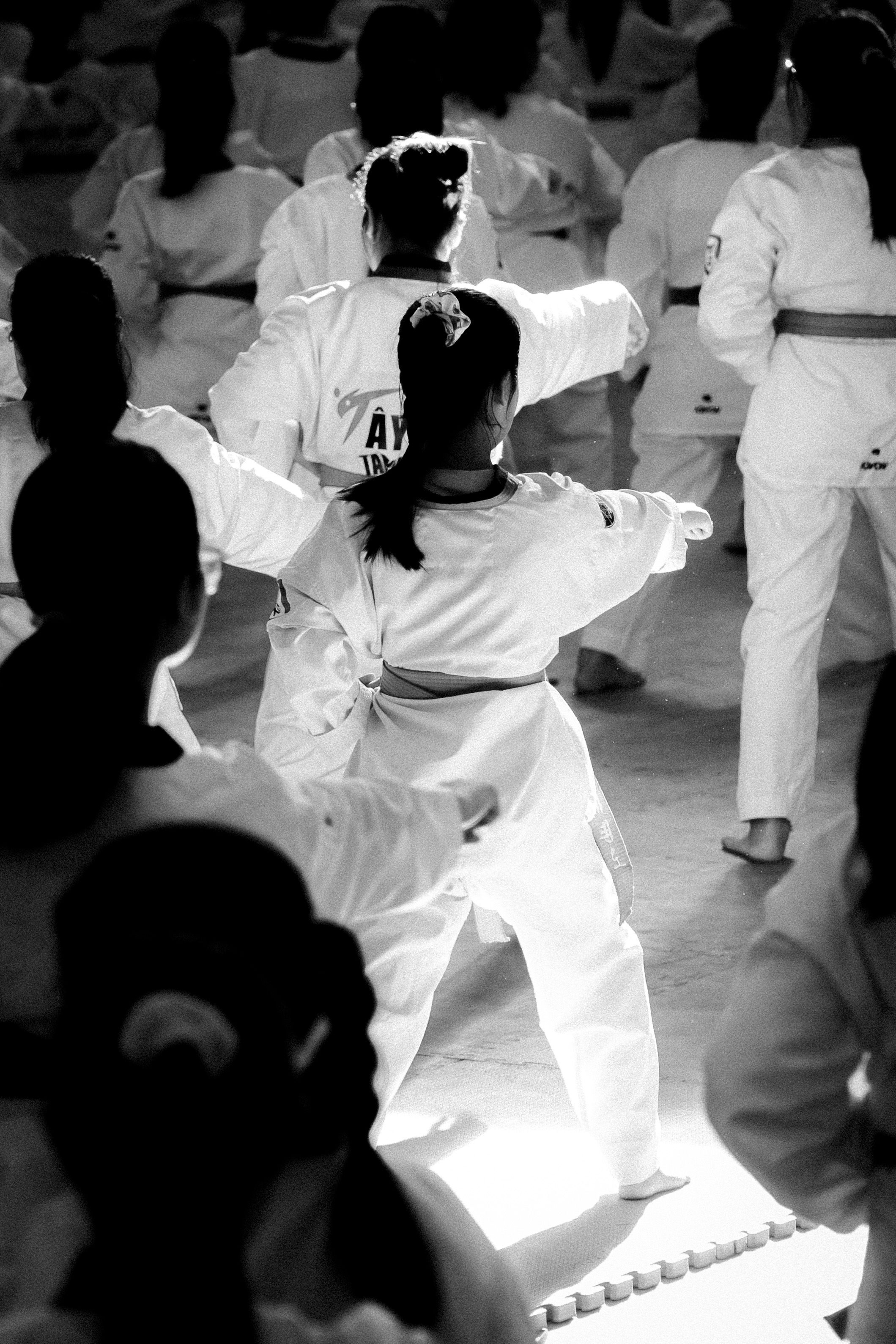 A group of karate students practicing in a well-lit training hall, captured in black and white.