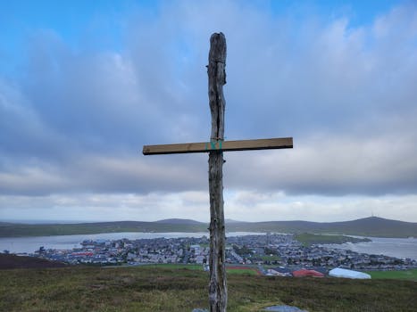 A scenic view of a wooden cross overlooking Lerwick, Scotland under a cloudy sky.