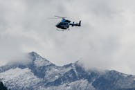 Blue Helicopter Flying over Snowy Mountain Peaks
