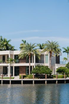 Modern luxury villa by the waterfront surrounded by palm trees, under a clear blue sky.