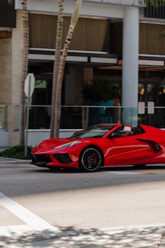 A striking red sports car with convertible top drives through a city street, capturing the essence of luxury and speed.