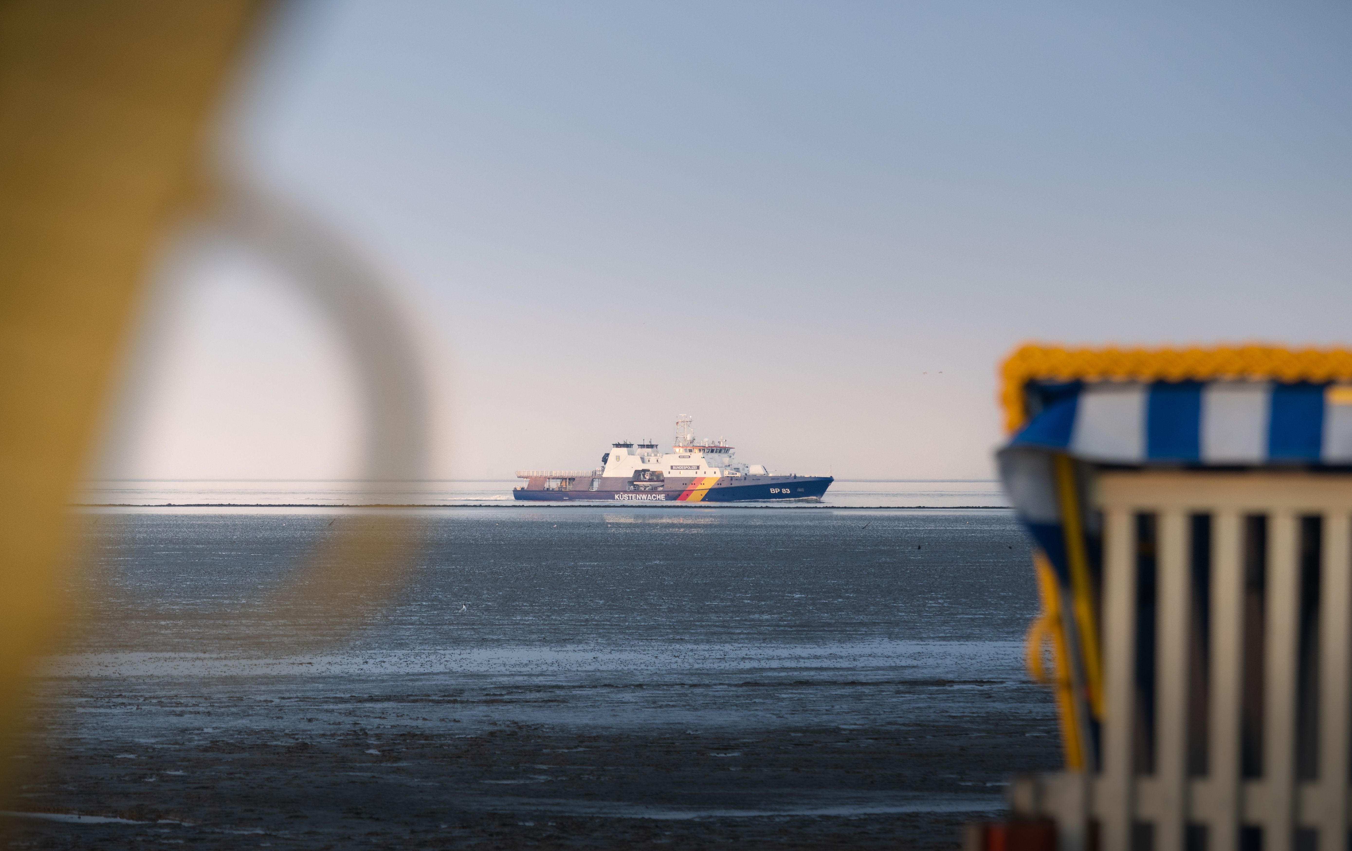 A ship sails on the North Sea near Cuxhaven, Germany, with beach chairs in the foreground.