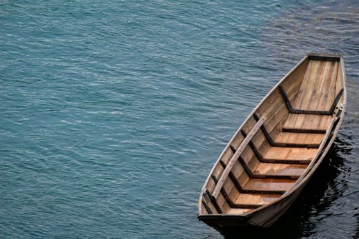 A wooden rowboat on calm blue water — Najm Shihabi on Pexels