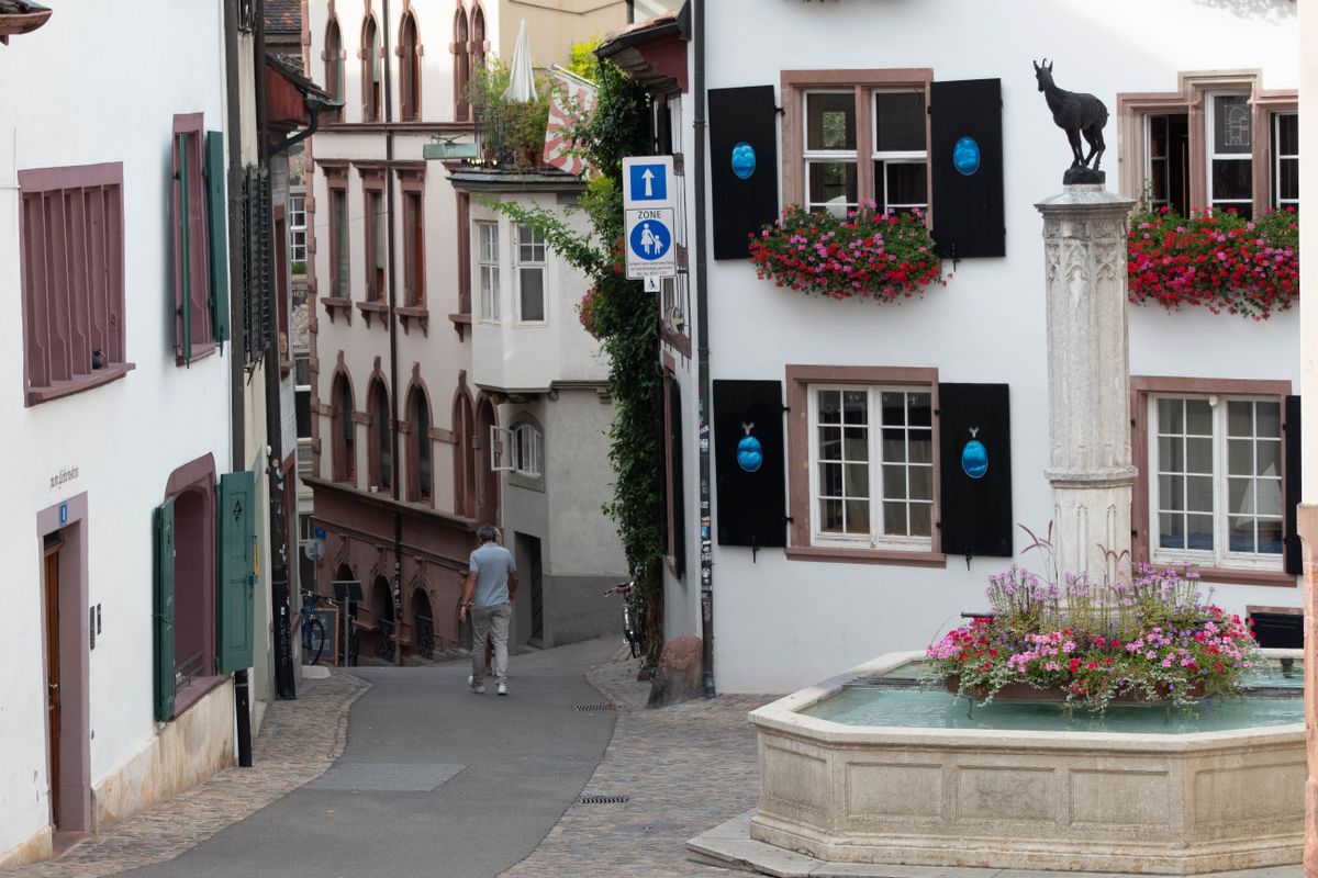 Alee îngustă din Basel, cu fântână de piatră și ferestre cu flori