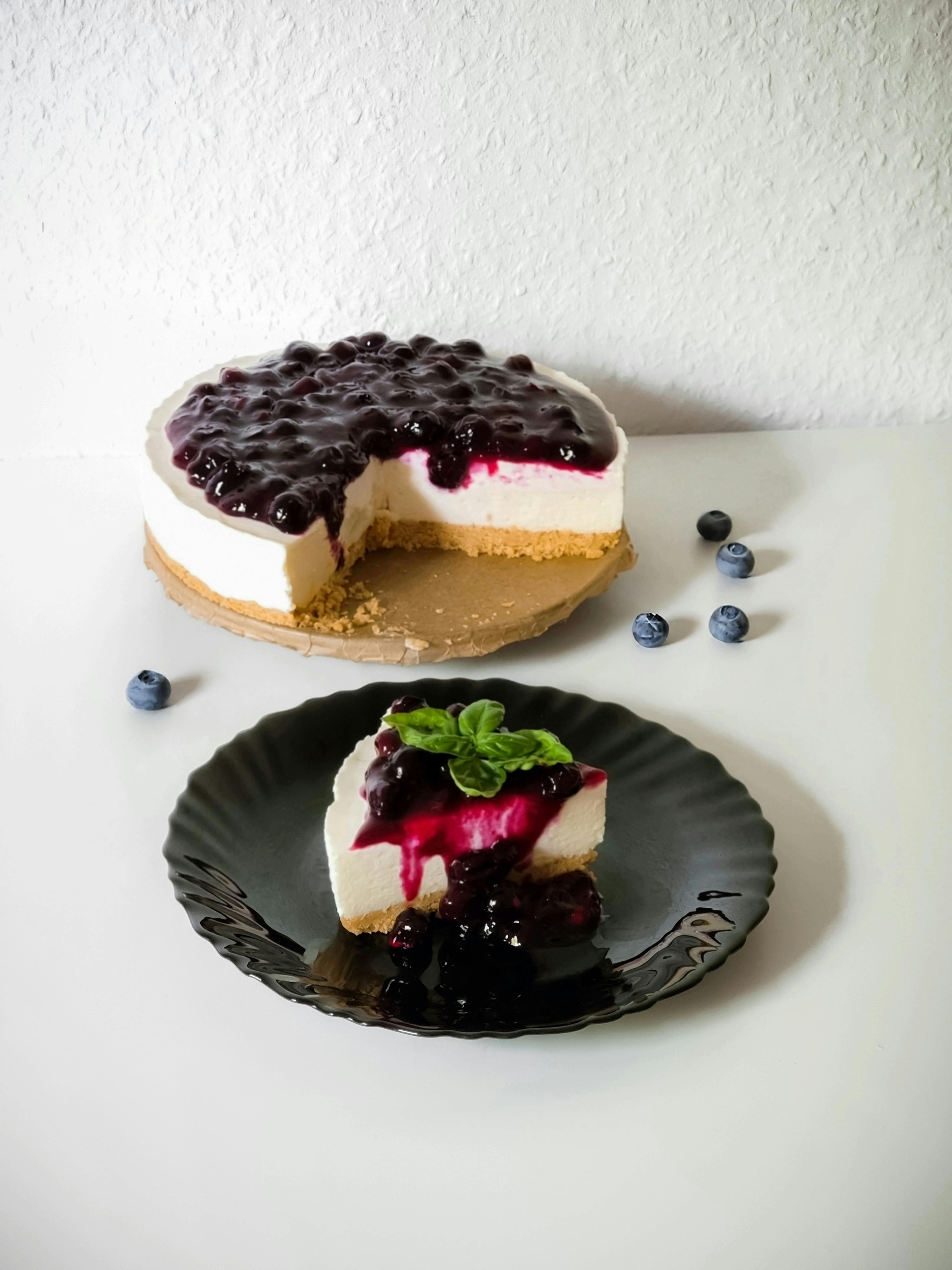 A sliced blueberry no-bake cheesecake on a black plate with whole cake in background.