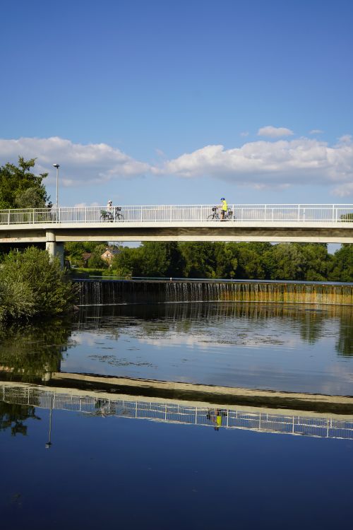 Free Peaceful scene of cyclists on a bridge above a river reflecting the clear blue sky in Horn-Bad Meinberg, Germany. Stock Photo