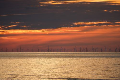 Free A breathtaking sunset over the ocean with an offshore wind farm silhouette, capturing sustainable energy against vibrant skies. Stock Photo
