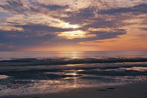 Free Peaceful beach scene at sunset with stunning cloud reflections in the water. Stock Photo