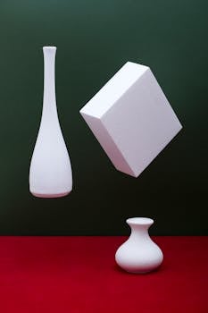 A balanced composition featuring white vases and a cube on red and green background.