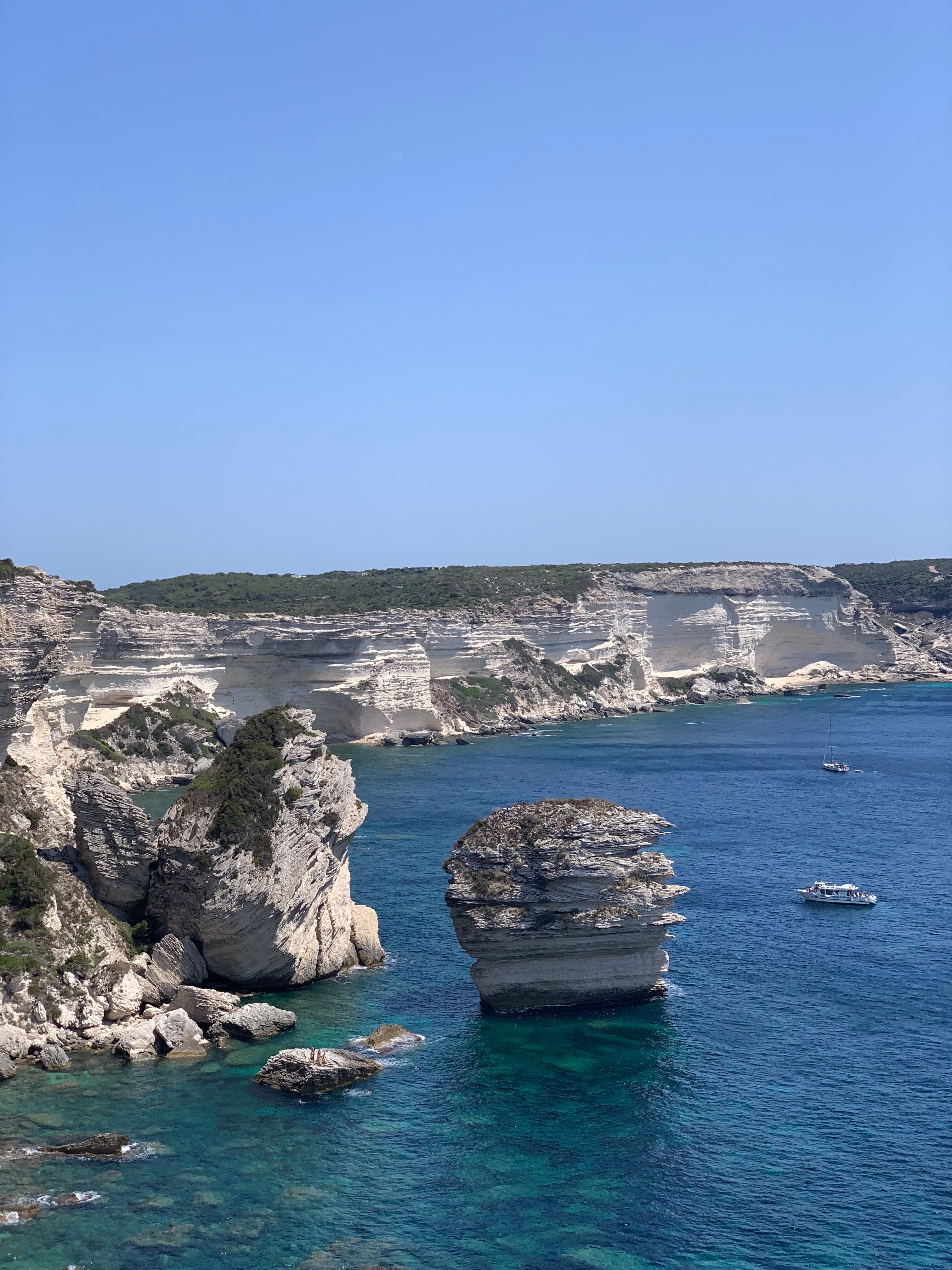 Breathtaking view of towering cliffs and clear blue waters in Bonifacio, Corse, France with boats.