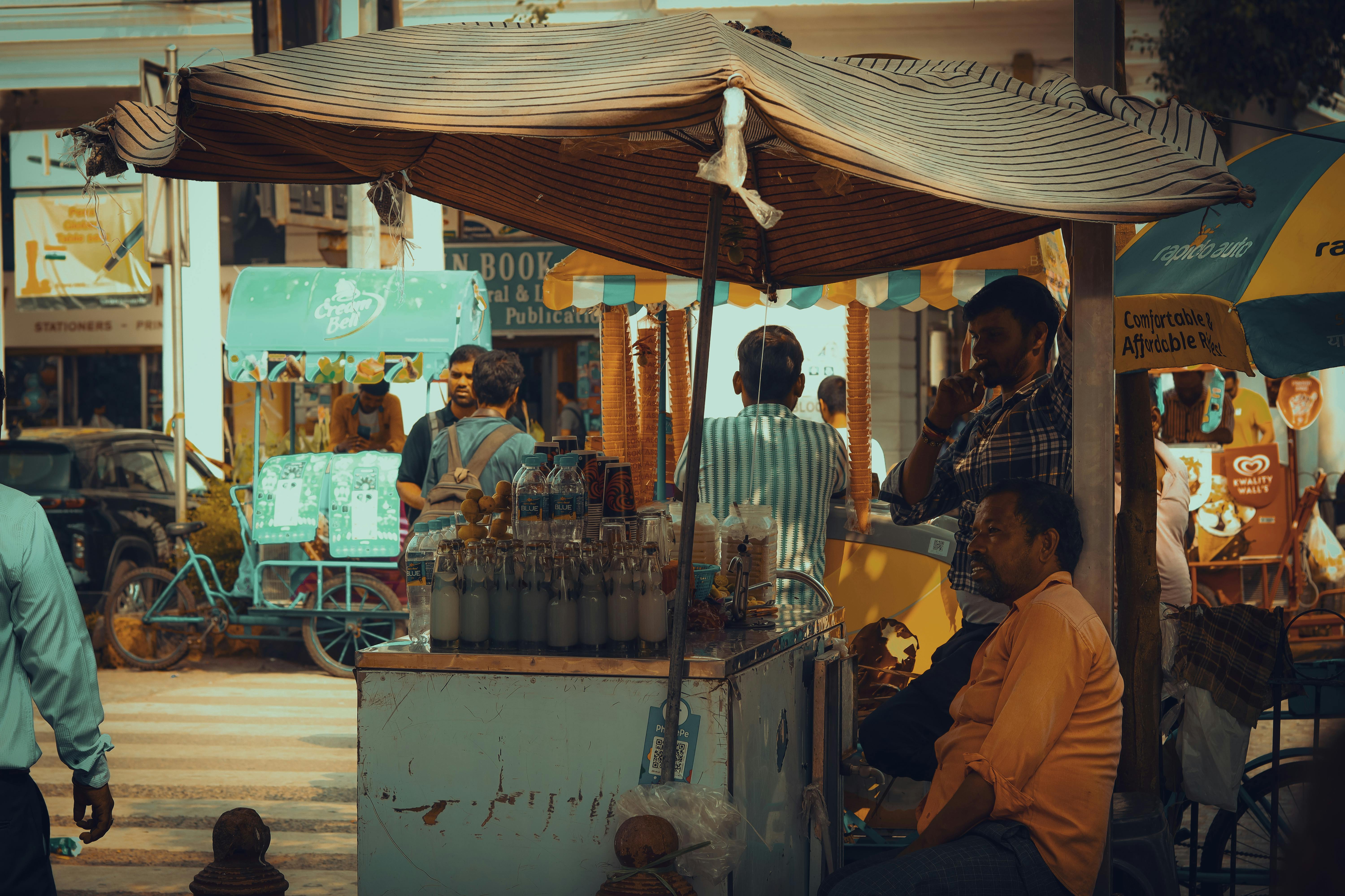 Vibrant street scene in Delhi with a busy refreshment stall and people enjoying local beverages.