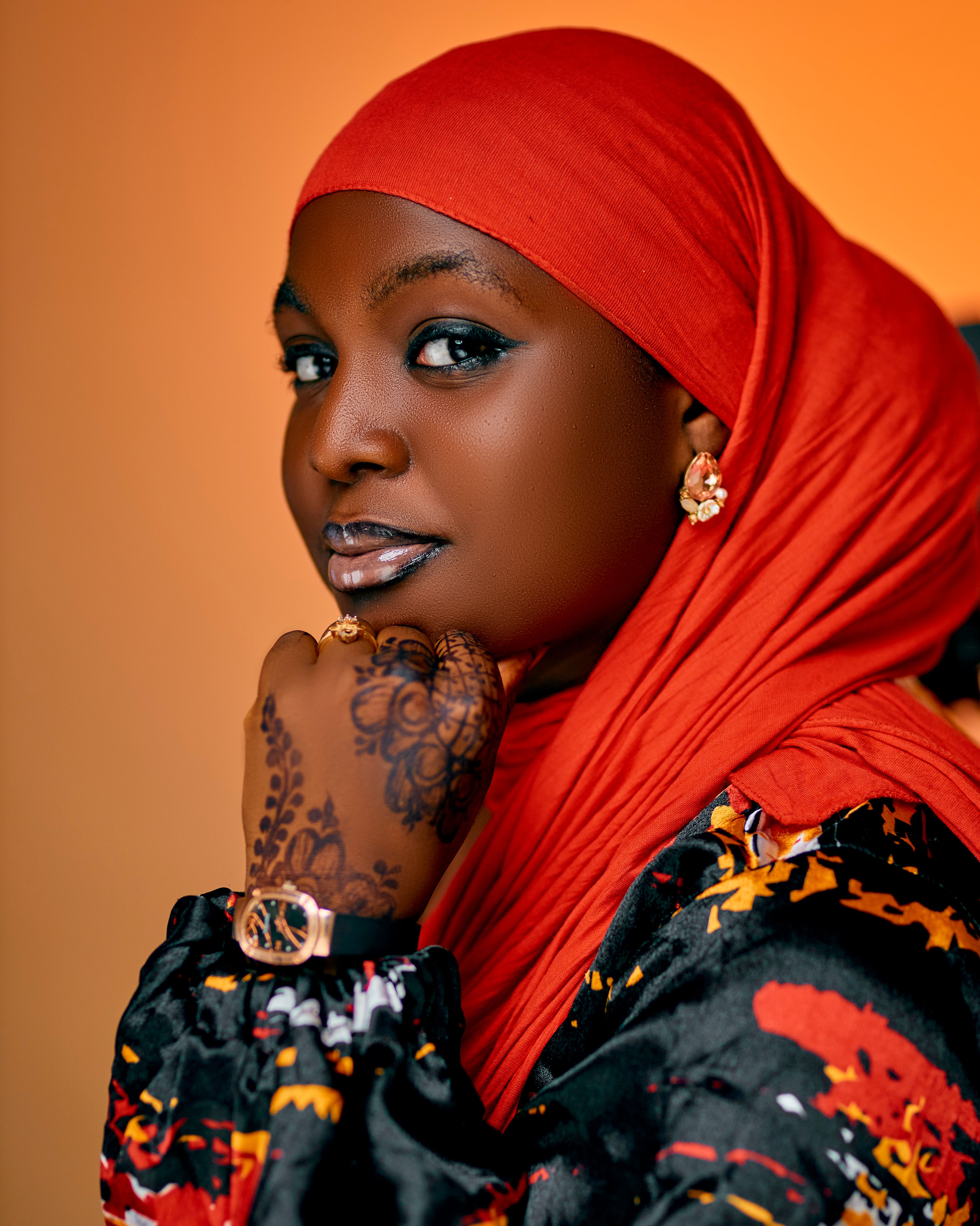 Portrait of a beautiful woman in a red hijab, showcasing intricate henna art and modern fashion.