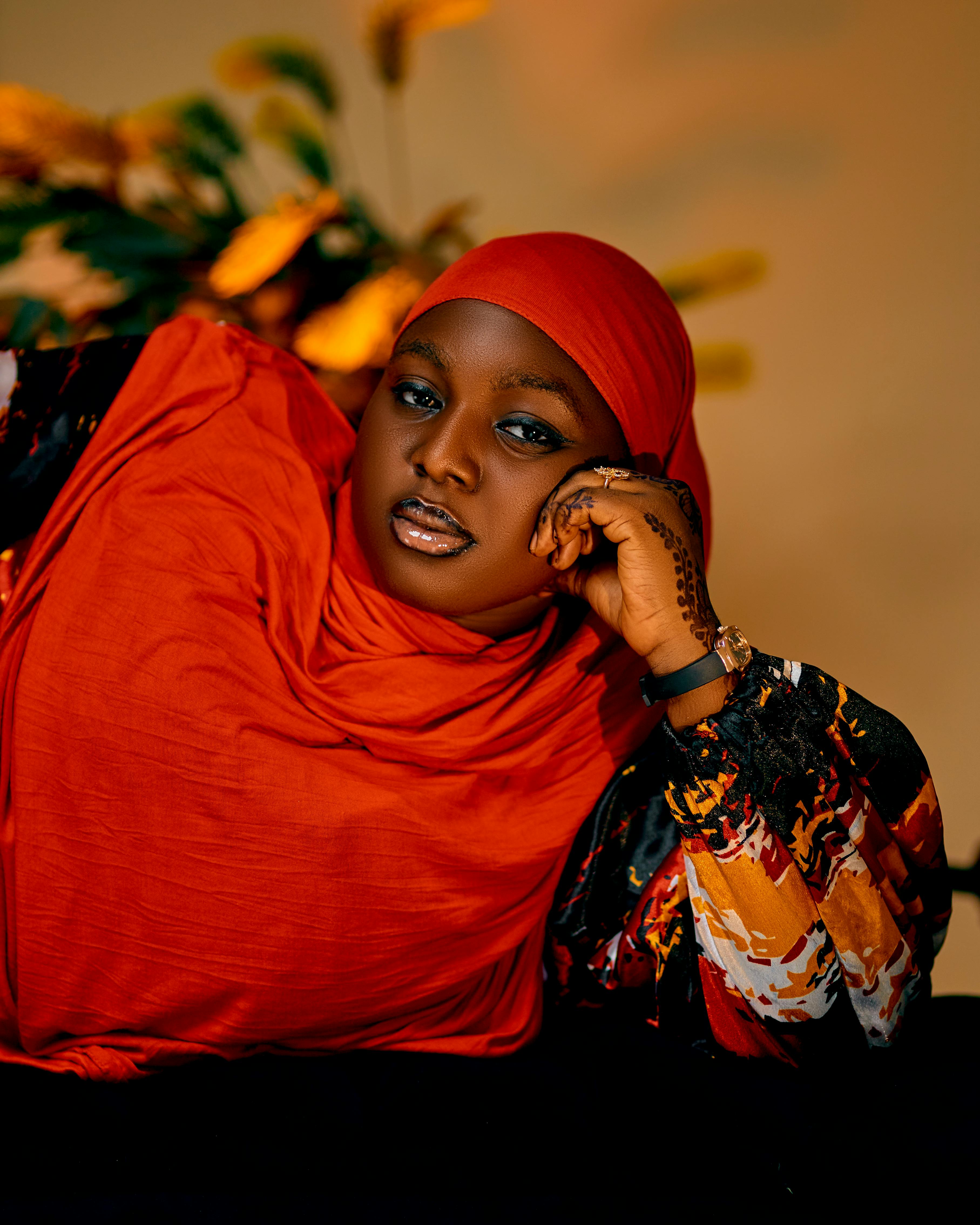 Confident woman wearing a vibrant red headscarf and patterned dress, posing indoors.