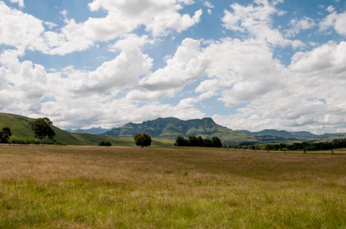 Free Beautiful view of the rolling hills and majestic Drakensberg mountains under a cloudy sky. Stock Photo