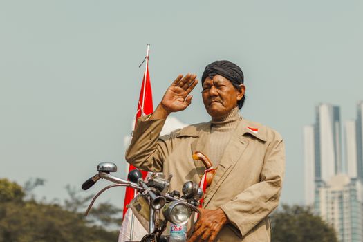 Elderly man with motorcycle saluting near urban skyscrapers, showcasing patriotism outdoors.