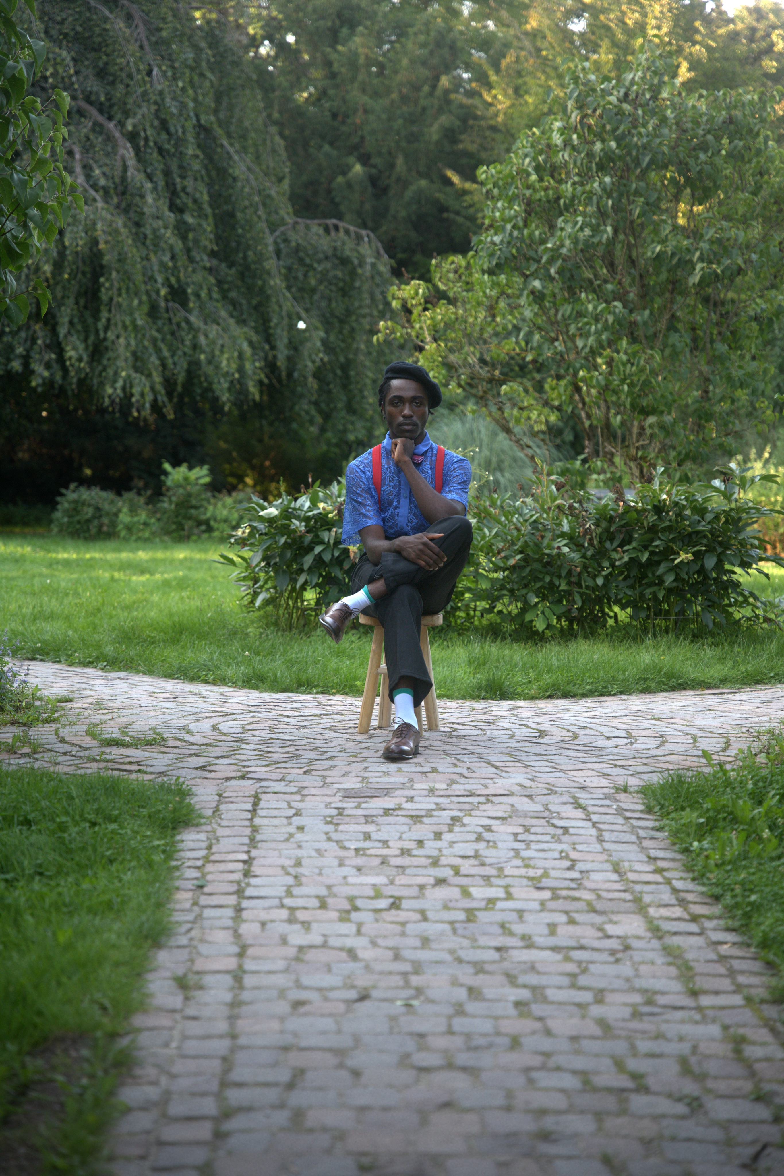 Man sitting thoughtfully on a chair in a lush green garden with cobblestone path.