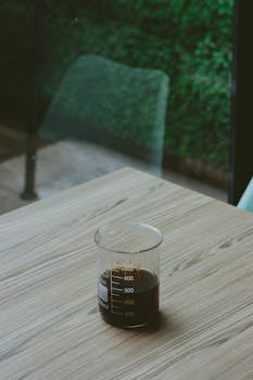 A unique presentation of coffee served in a glass beaker on a wooden table in a cozy café.