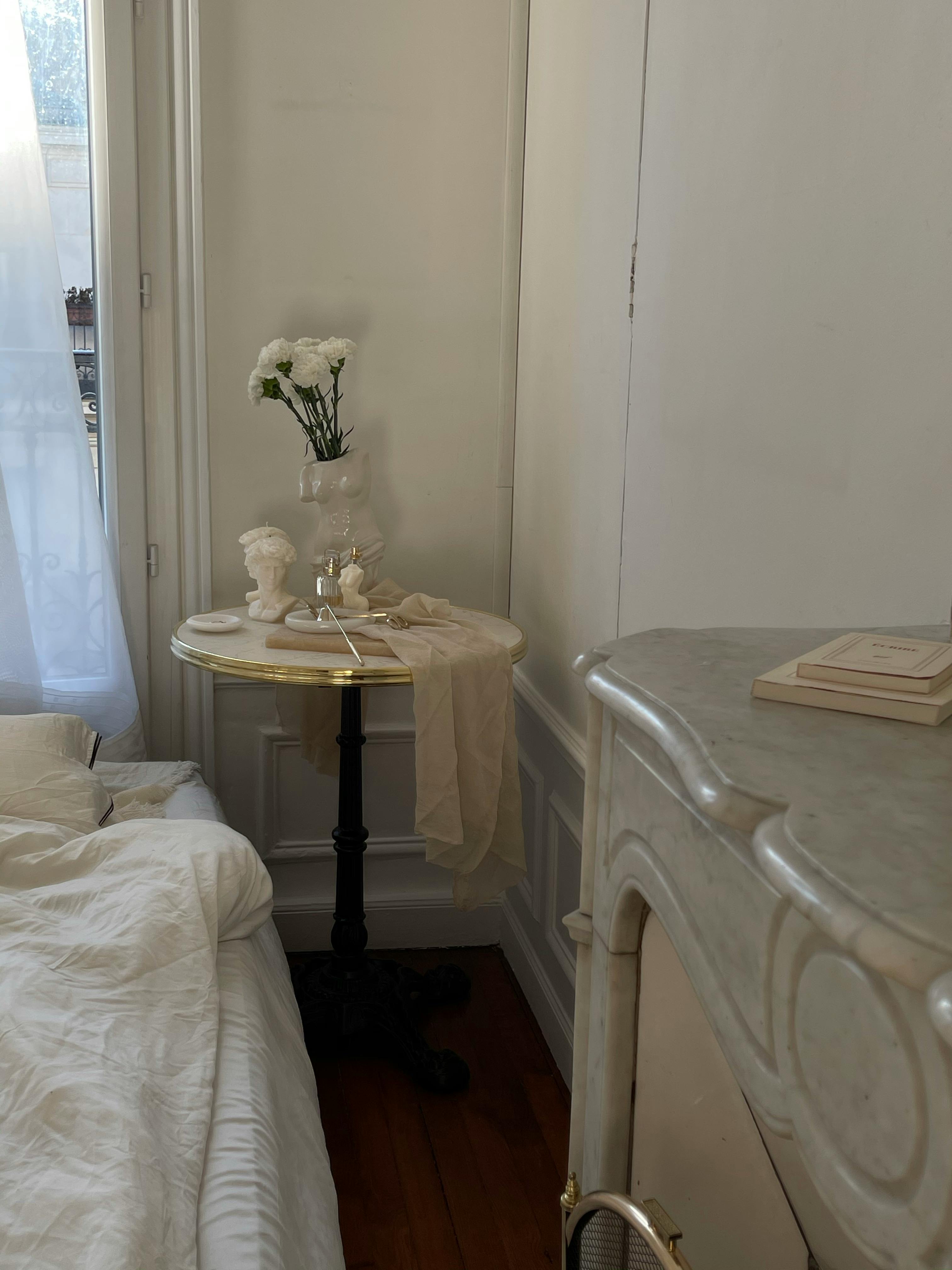 Cozy bedroom corner featuring a side table with flowers, classic decor, and warm lighting.