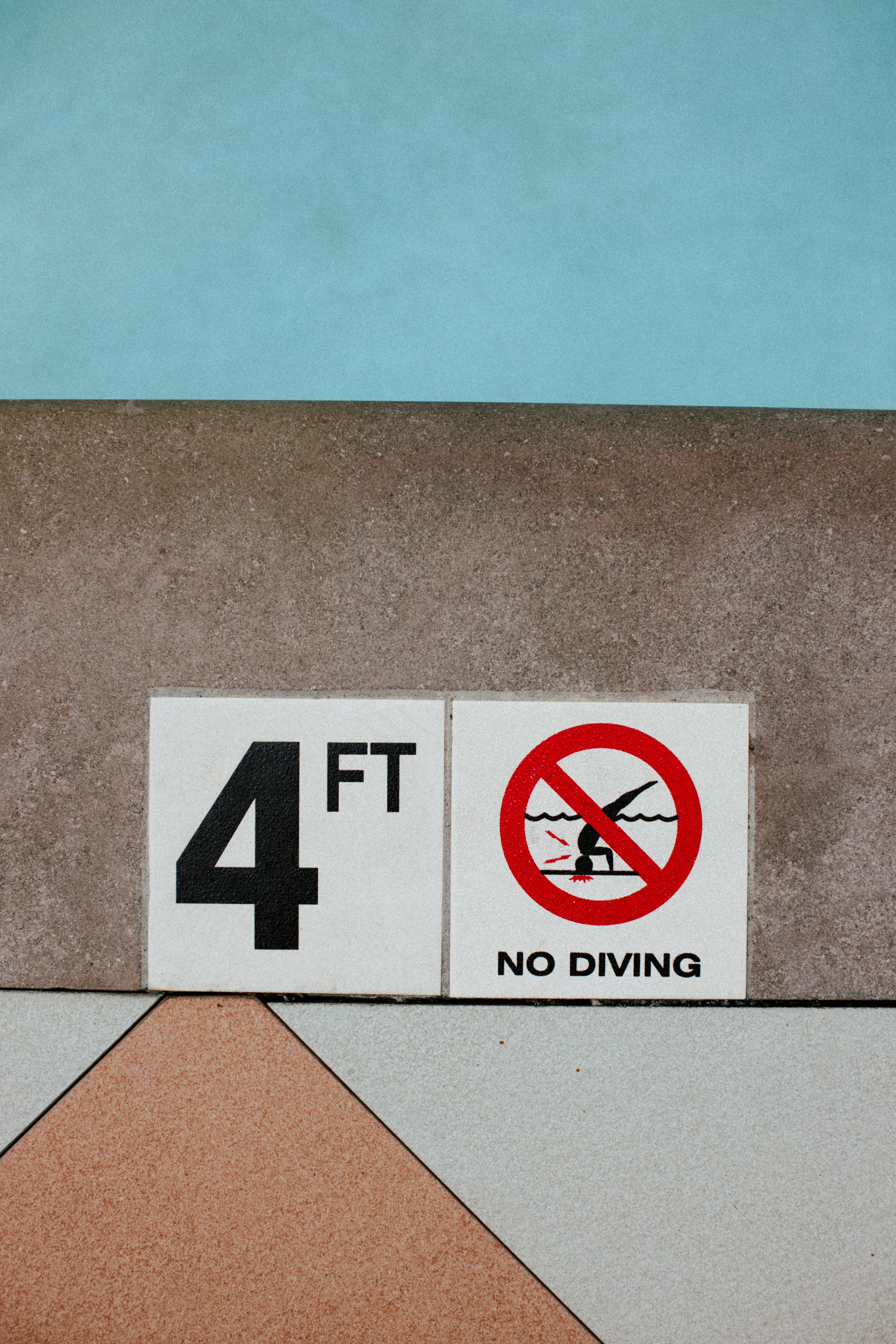 Close-up of a 4-foot depth warning and no diving sign at a pool edge.