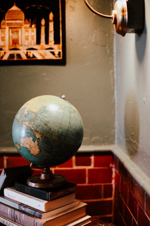 Free A classic vintage globe rests on stacked books in a warmly lit cozy corner with artwork. Stock Photo