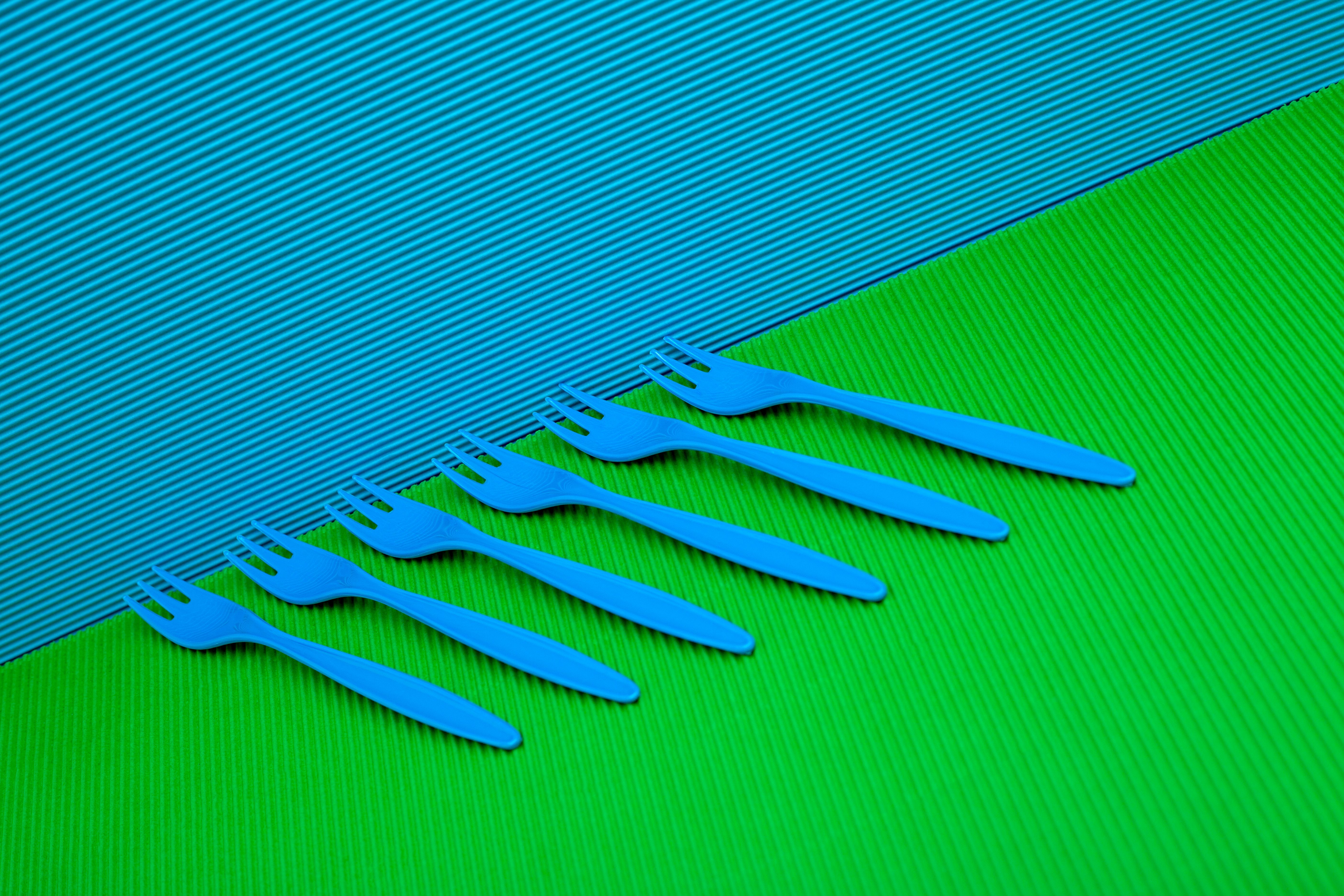 Six blue plastic forks arranged on a bright green and blue background. Modern and minimalist style.