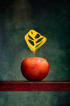 A red apple with a creatively carved yellow leaf on a wooden shelf, artistic shot.