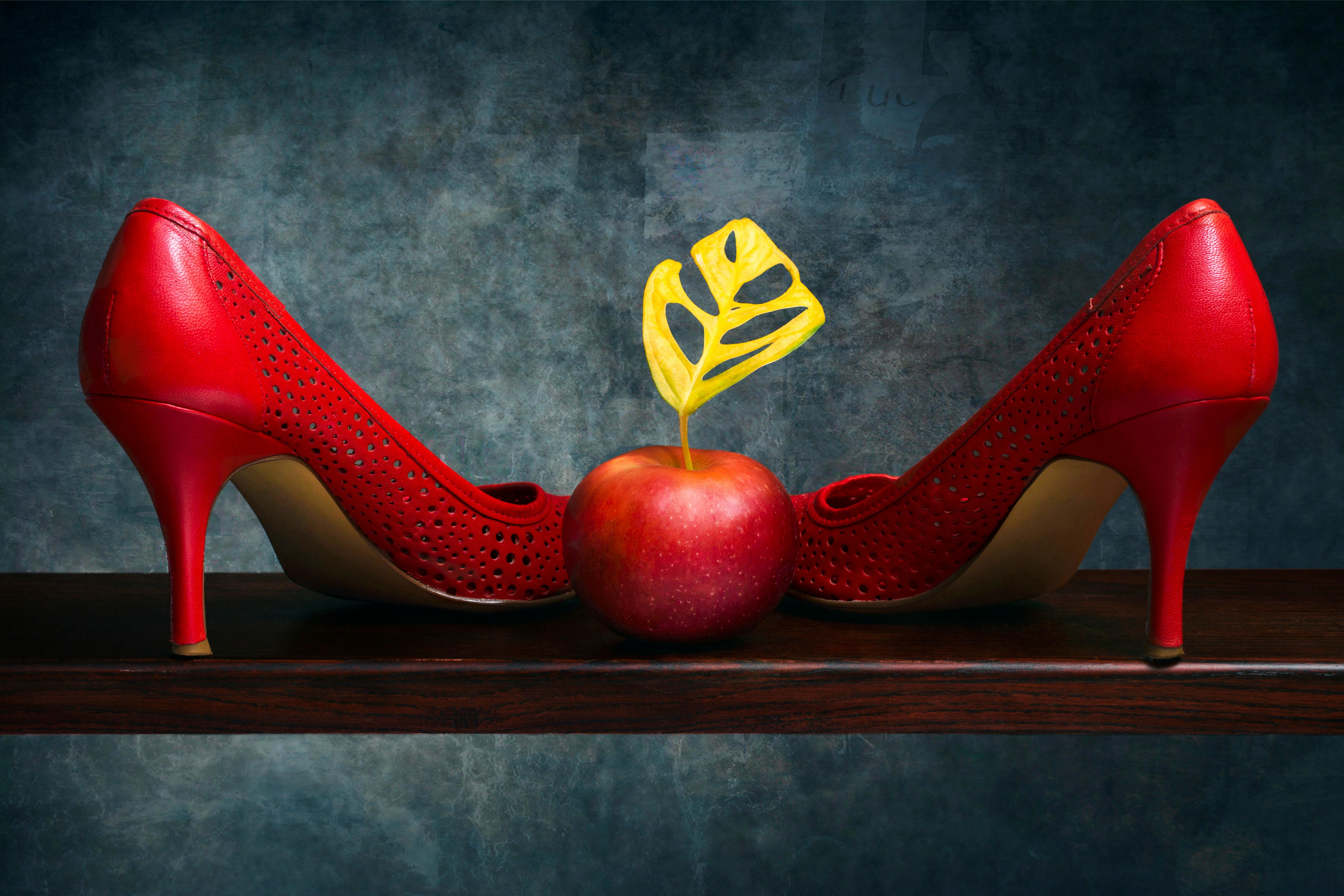 Artistic still life of red high heels and apple on a wooden shelf.