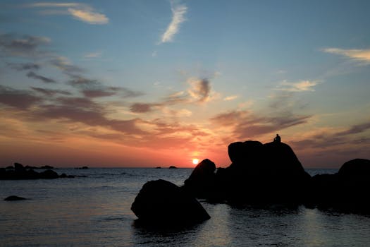 A serene sunset view over the sea with a solitary silhouette on rocks in Bretagne, France.