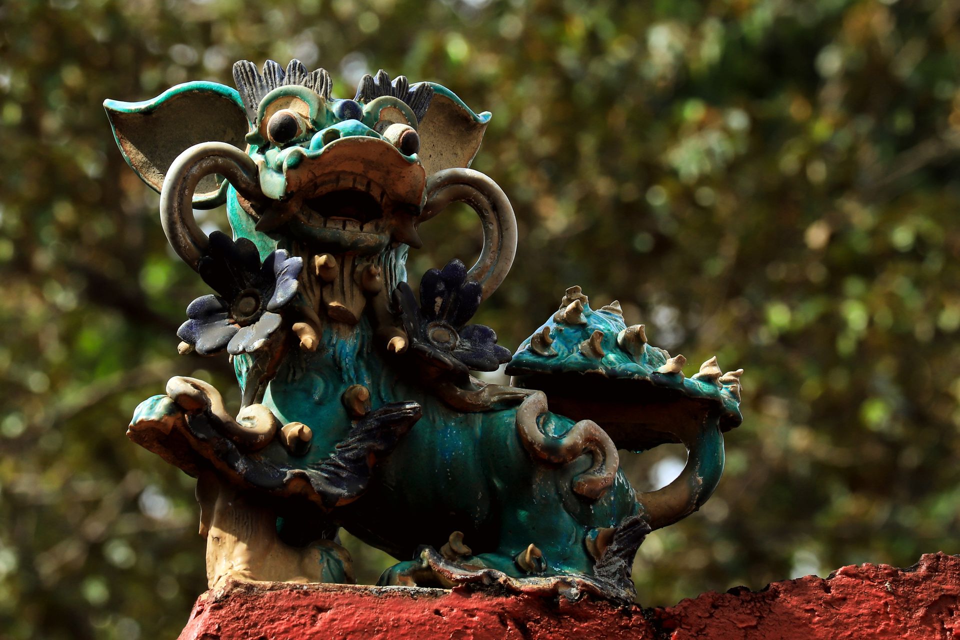 An ornate dragon statue on a red wall outdoors, showcasing intricate artistry.